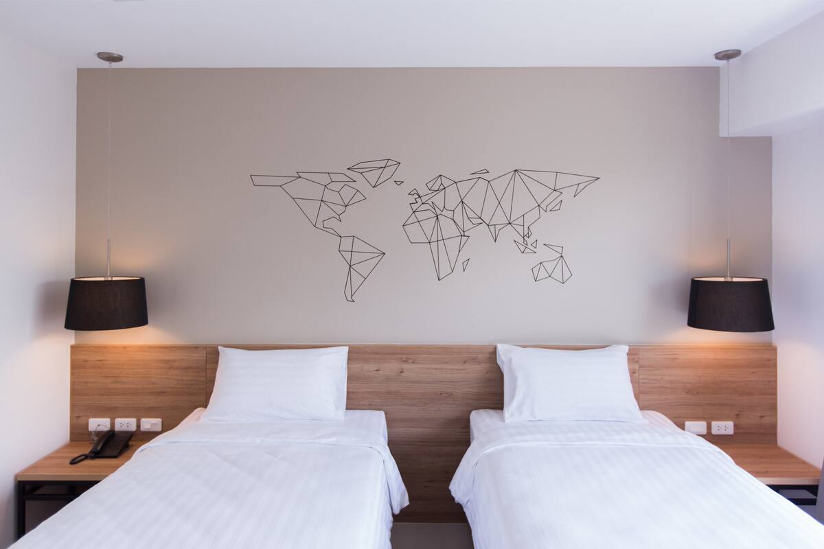 Habitación de hotel con dos camas, un cuadro con un mapa del mundo en la pared y dos lámparas de noche.