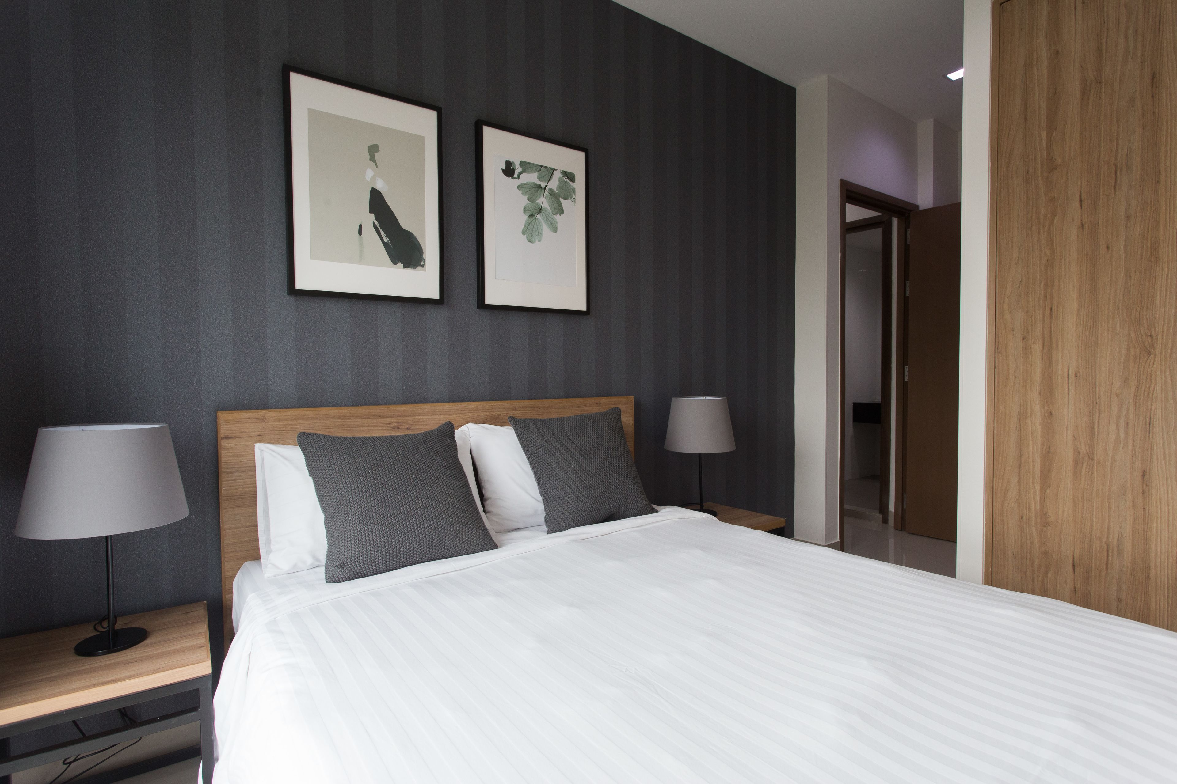 A modern hotel room with a large bed, two bedside tables with lamps, and framed artwork on the wall.