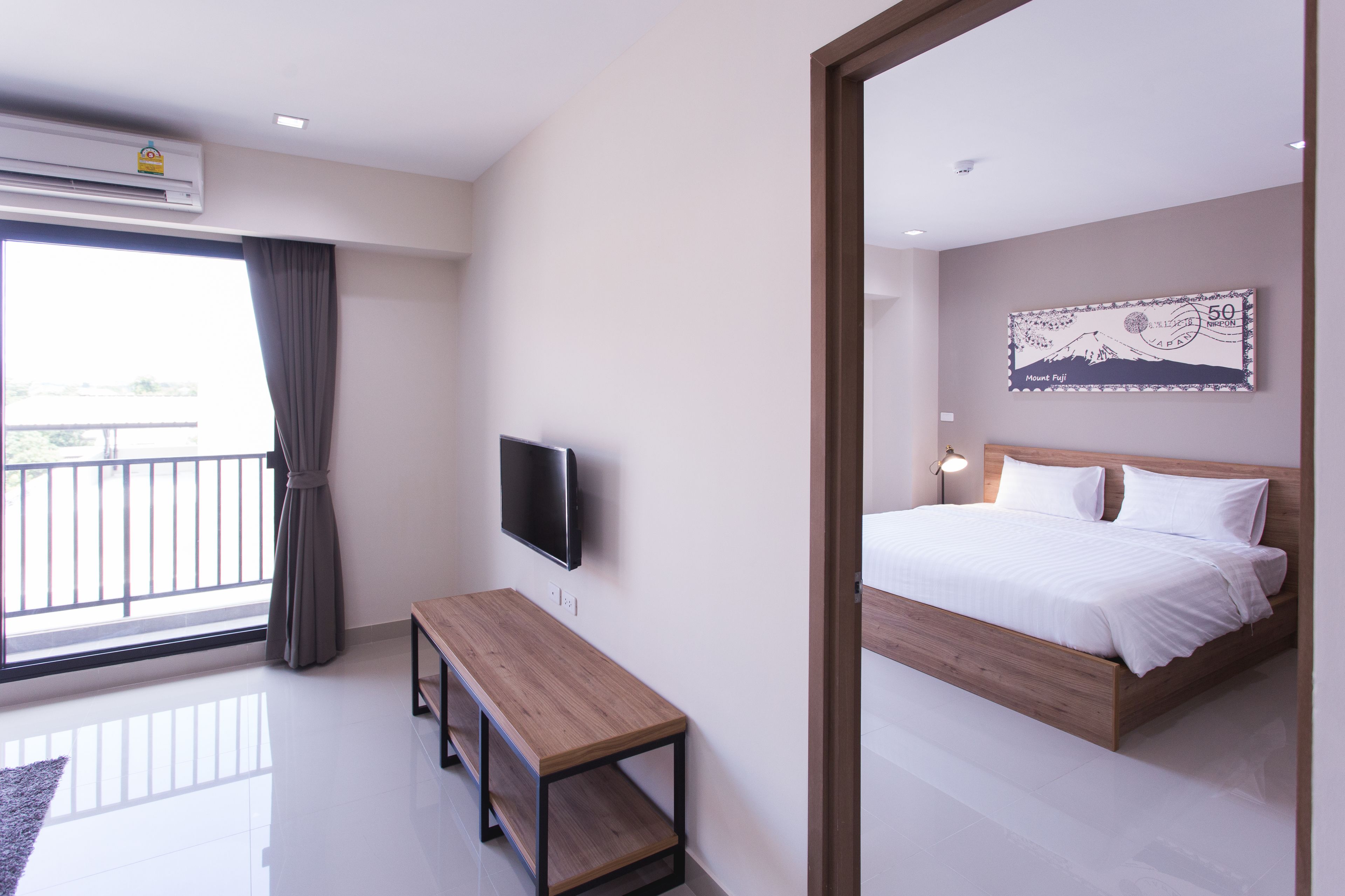 A modern hotel room with a large bed, a flat-screen TV mounted on the wall, a wooden bench, and a large window with a view of a balcony.