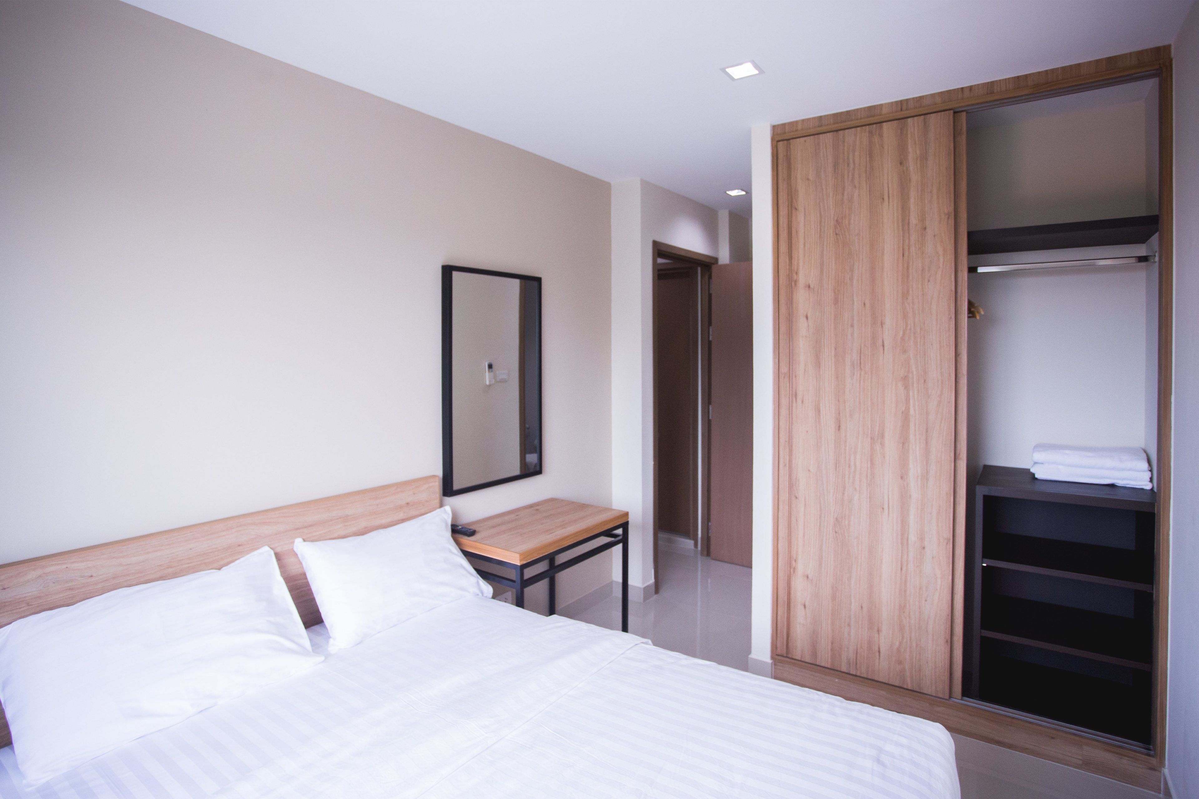 A modern hotel room with a wooden bed frame, a bedside table, a large mirror, and a walk-in closet with shelves.
