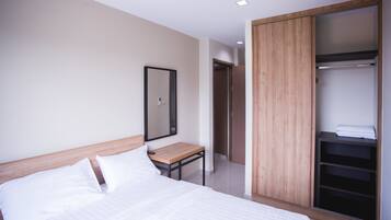 A modern hotel room with a wooden bed frame, a bedside table, a large mirror, and a walk-in closet with shelves.