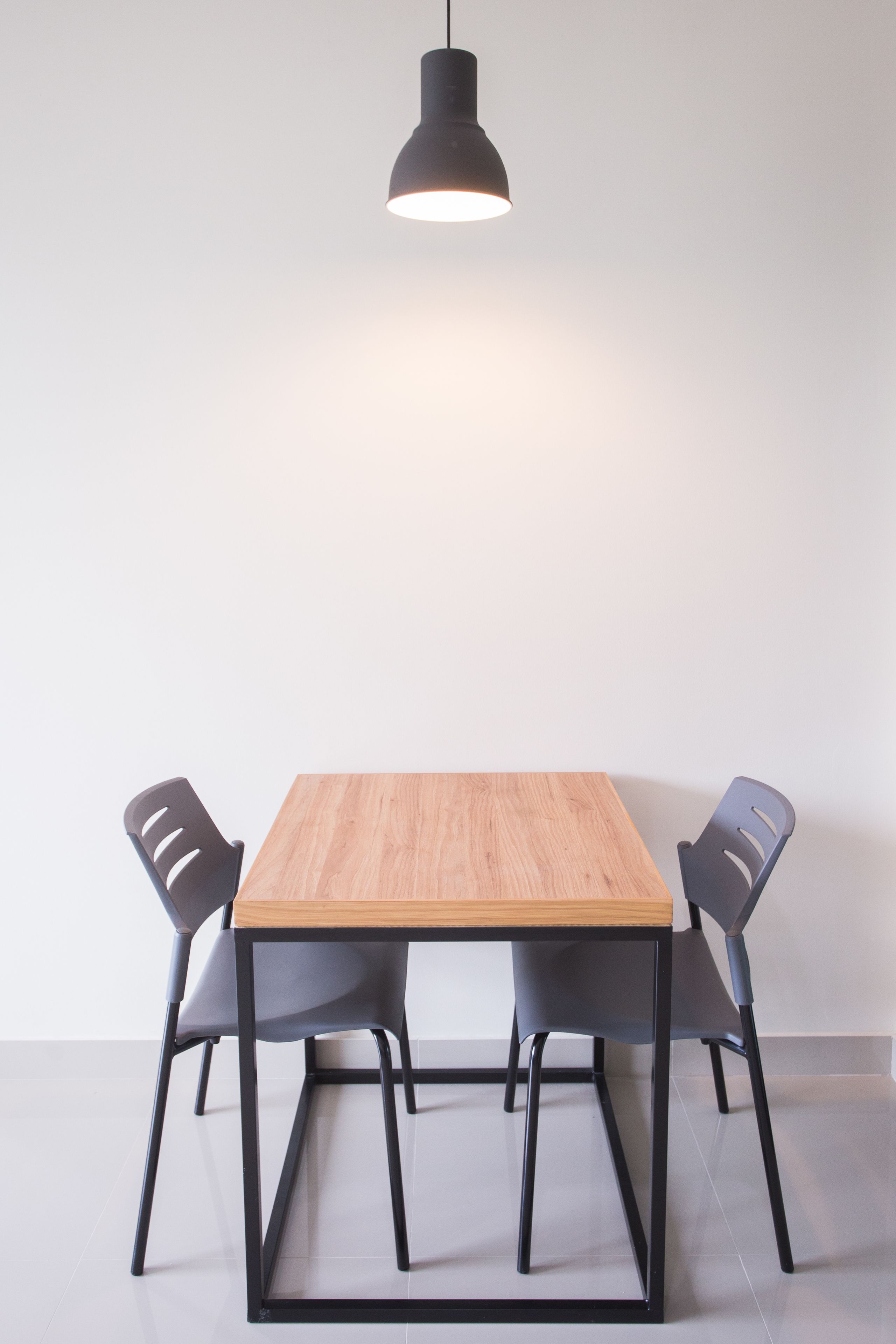 A dining table with a wooden top and black metal frame, flanked by two grey chairs with cut-out backrests.