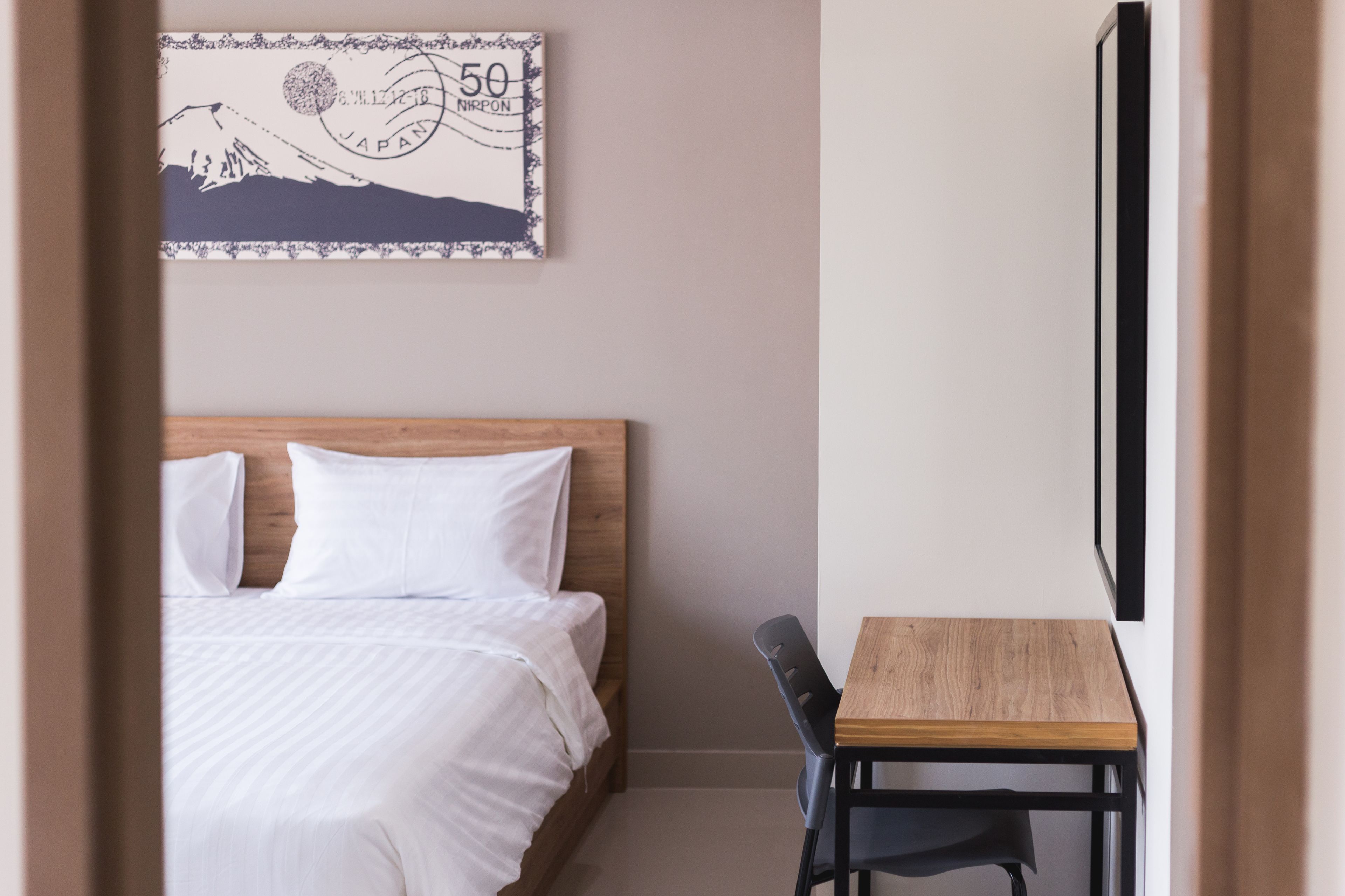 Ett hotellrum med en säng, ett skrivbord i trä och en tavla som hänger på väggen, föreställande ett berg och ett frimärke.
