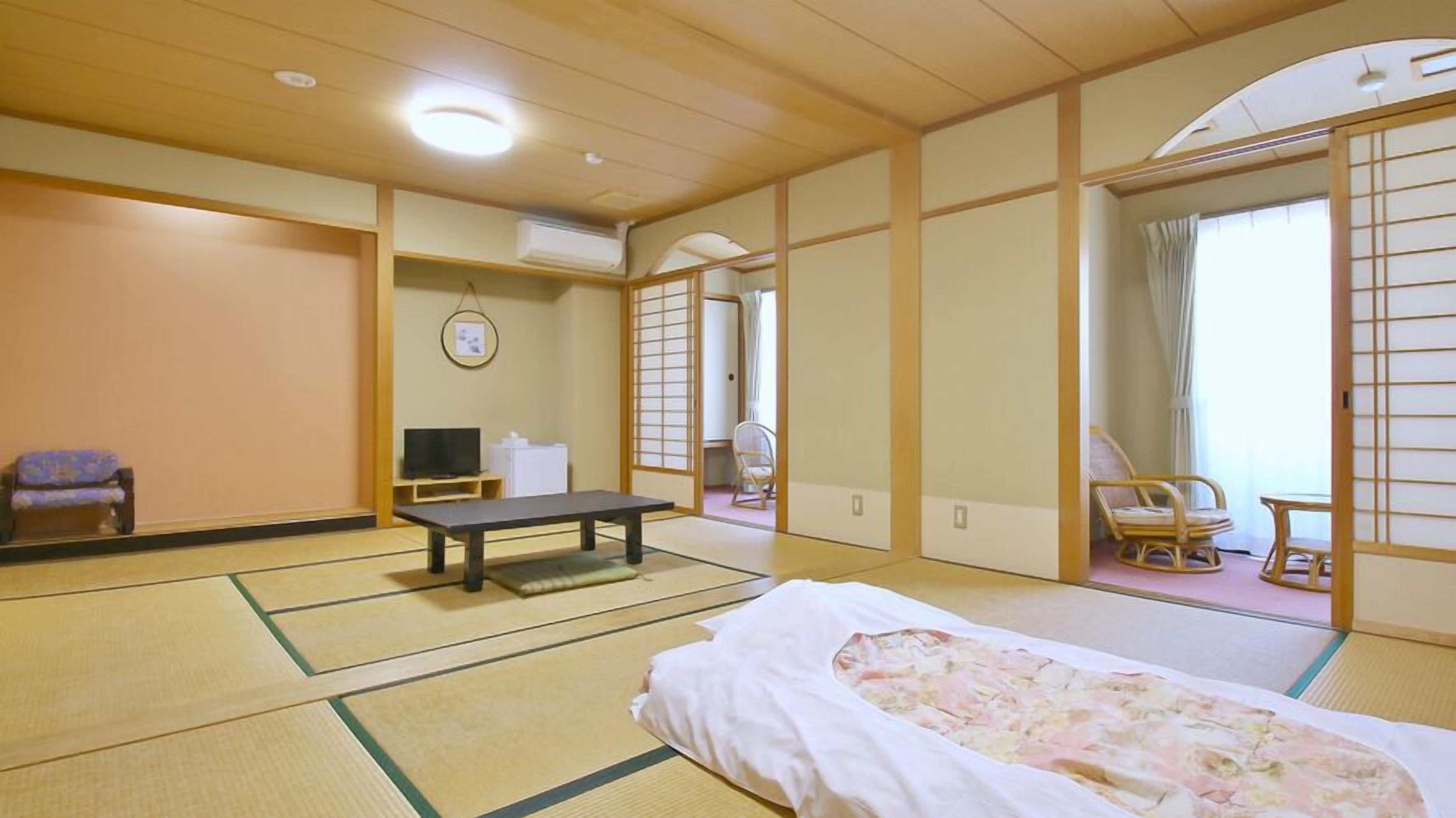 Une pièce de style japonais traditionnel, avec un sol recouvert de tatamis, un futon servant de lit, une petite table basse, un téléviseur et une porte coulissante donnant sur une autre pièce.