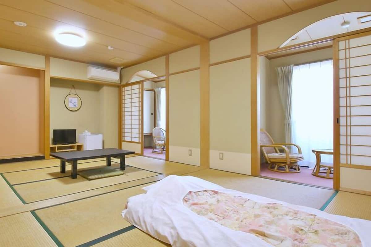 Une pièce de style japonais traditionnel, avec un sol recouvert de tatamis, un futon servant de lit, une petite table basse, un téléviseur et une porte coulissante donnant sur une autre pièce.