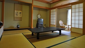 Una habitación con esteras de tatami, una mesa baja, un televisor, un pergamino de caligrafía japonesa tradicional y un biombó shoji.