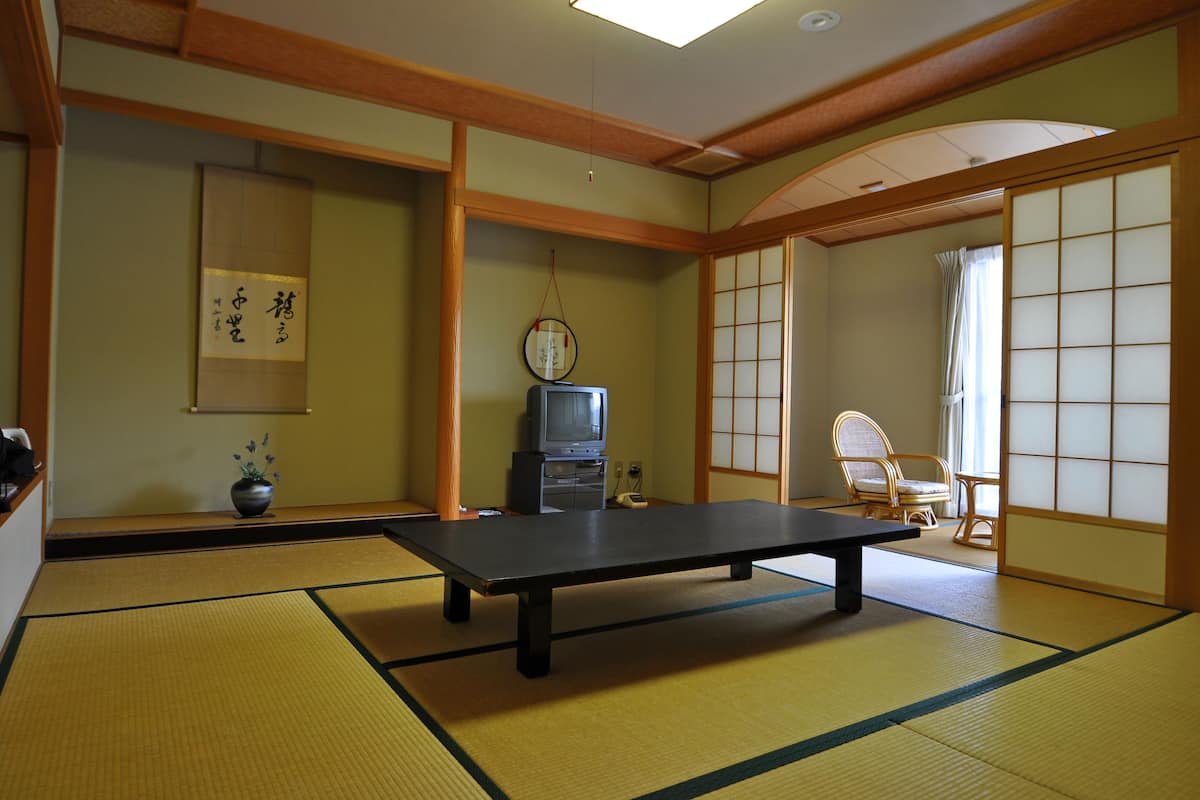Une pièce avec un sol recouvert de tatamis, une petite table basse, un téléviseur, un rouleau de calligraphie japonaise traditionnelle et un paravent shoji.
