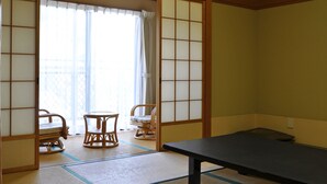 Una habitación japonesa tradicional con suelo de tatami, una mesa baja, dos sillas y un fusuma corredizo.
