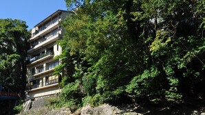 Un edificio de varios pisos con balcones, rodeado de abundante vegetación y un río.