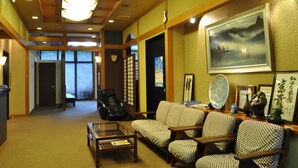 Una habitación tradicional japonesa con suelo de tatami, una mesa baja, un sofá y una silla.