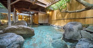 A traditional Japanese onsen with a wooden interior, a stone bath surrounded by rocks, and a wooden ceiling structure. - Misasa Royal Hotel (Misasa)