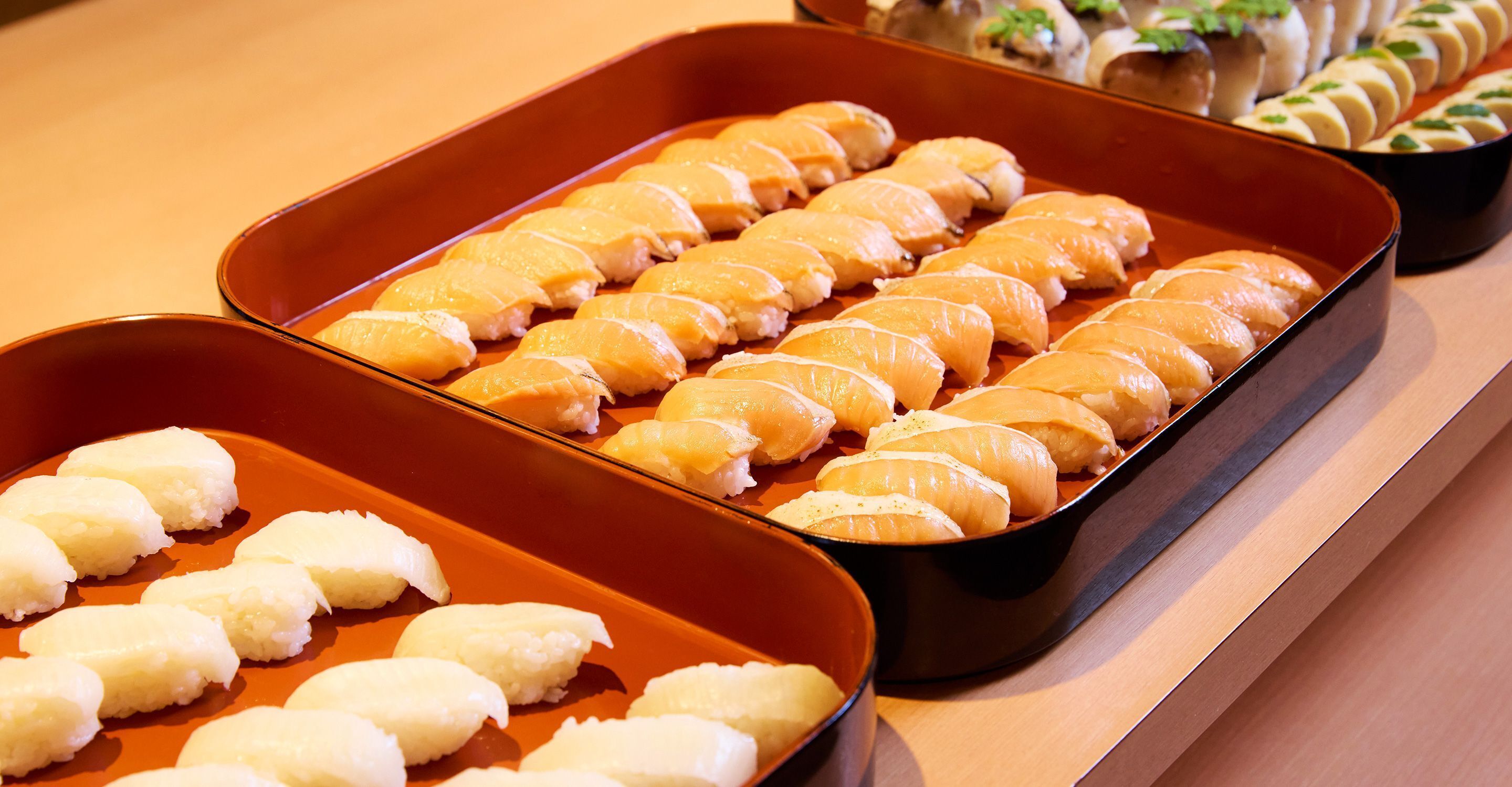 Variedad de sushi dispuesto cuidadosamente en dos bandejas rectangulares sobre una mesa de madera.