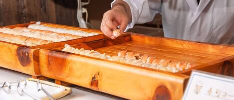 A person preparing sushi at a wooden counter with multiple trays of sushi.