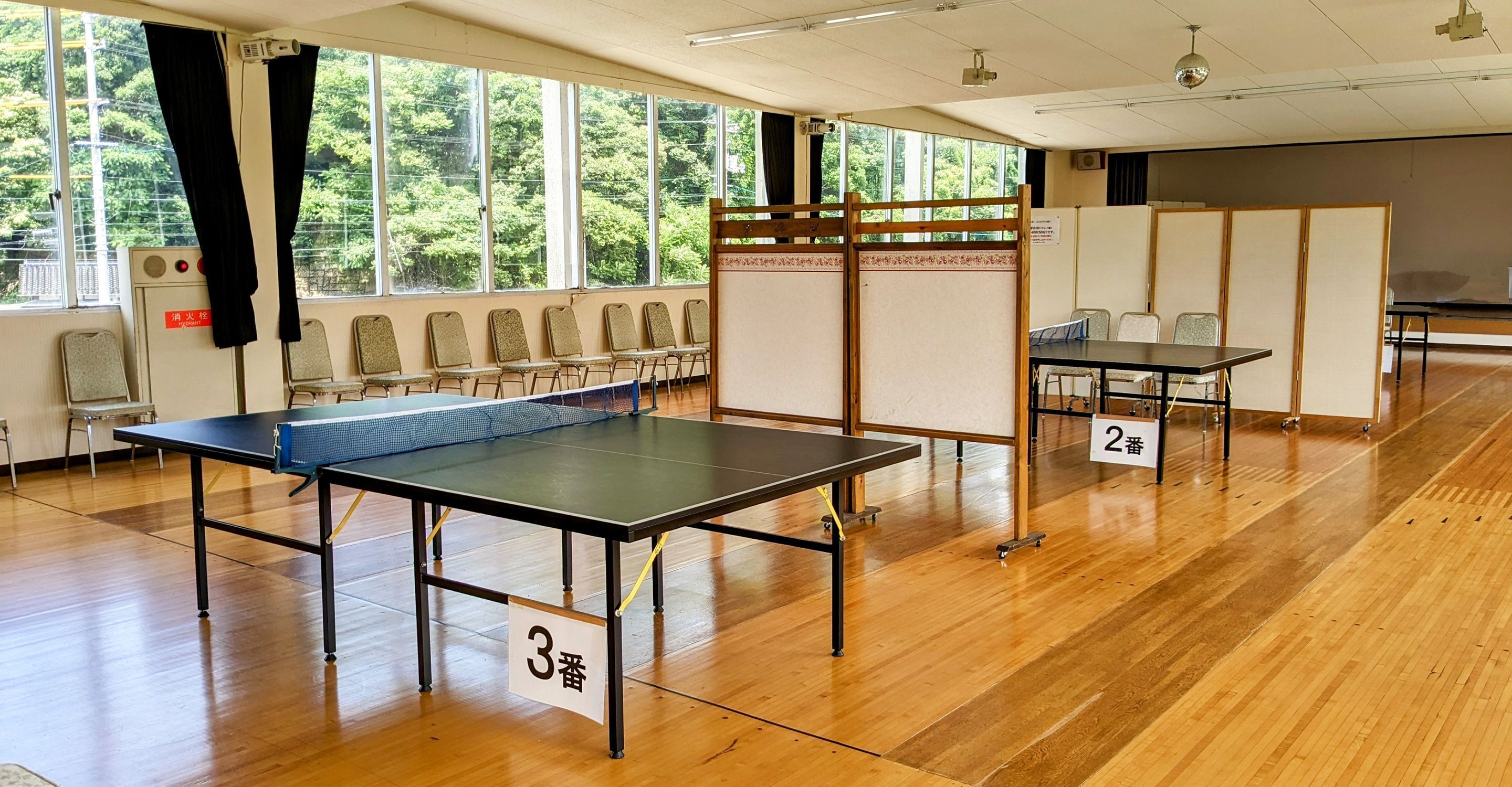 Una habitación con dos mesas de ping pong, numeradas 2 y 3, y un área de estar con sillas.
