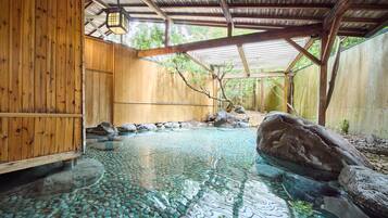 A traditional wooden bathhouse with a clear stone pool, wooden benches, and a rustic interior.