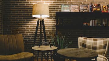 A cozy seating area with a brick wall, a floor lamp, a bookshelf with books, and a potted plant.