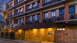 A multi-story hotel with balconies, a well-lit entrance, and a brick facade. - Sakura Terrace The Atelier (Kyoto)