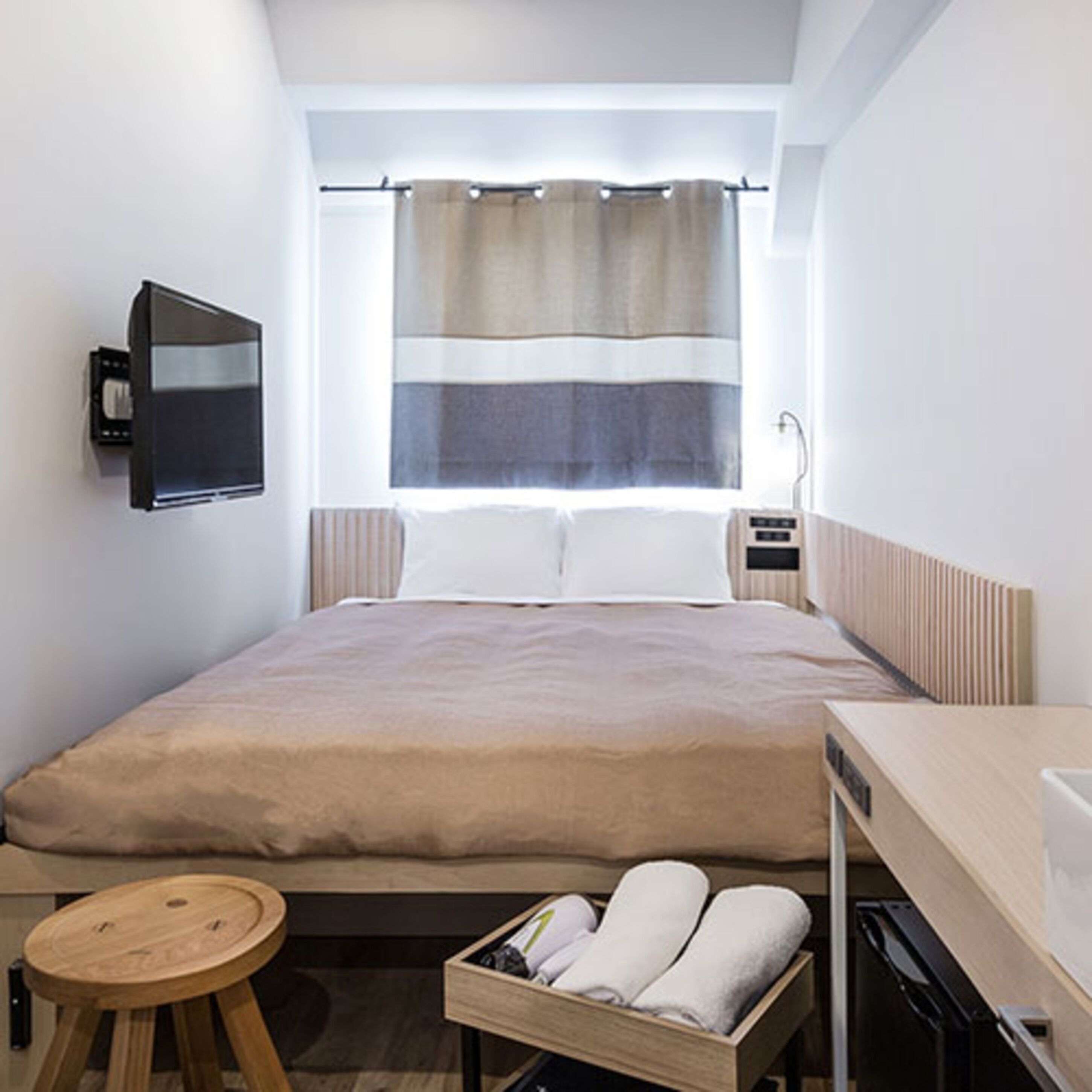 A modern hotel room with a large bed, a bedside table, a TV mounted on the wall, and a window with curtains.