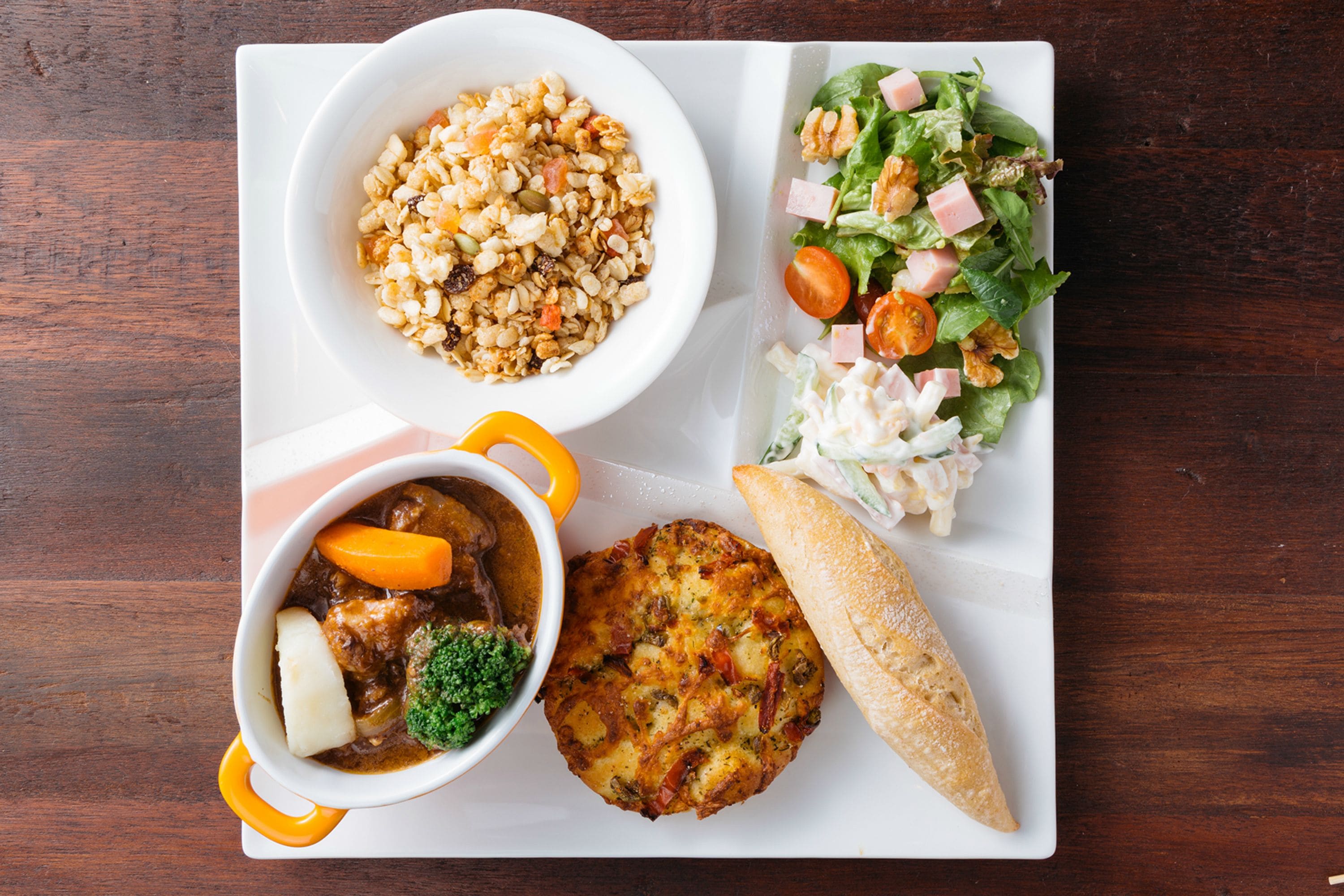 A meal consisting of a bowl of soup, a salad, a piece of bread, and a small pastry on a white plate.