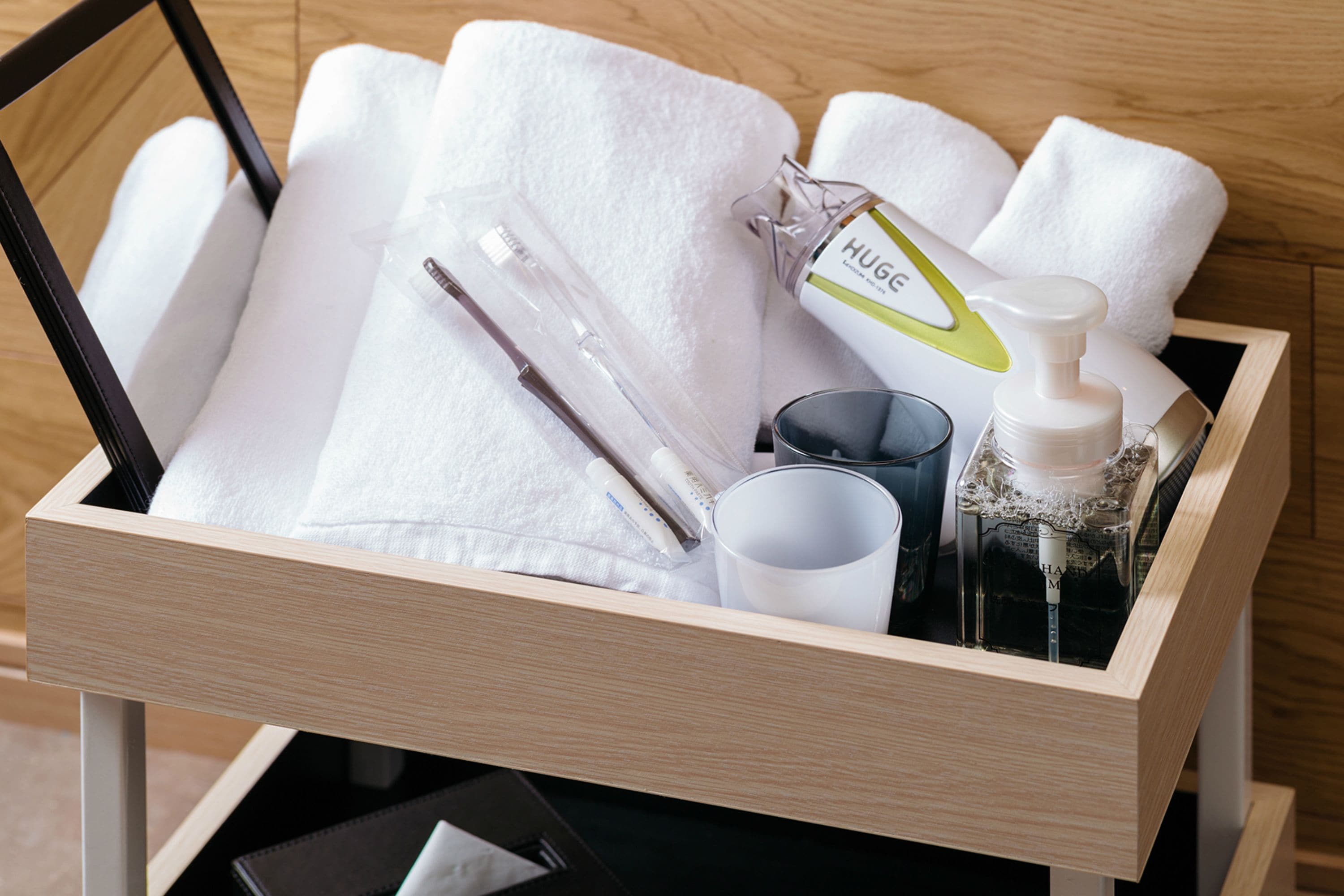 A wooden drawer containing a white towel, a glass of water, a white bottle with a pump, a black pen, and a white cup.