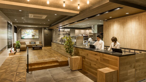 A modern reception area with a wooden reception desk, seating area with a sofa and coffee table, and a large abstract painting on the wall. - Sakura Terrace The Atelier (Kyoto)