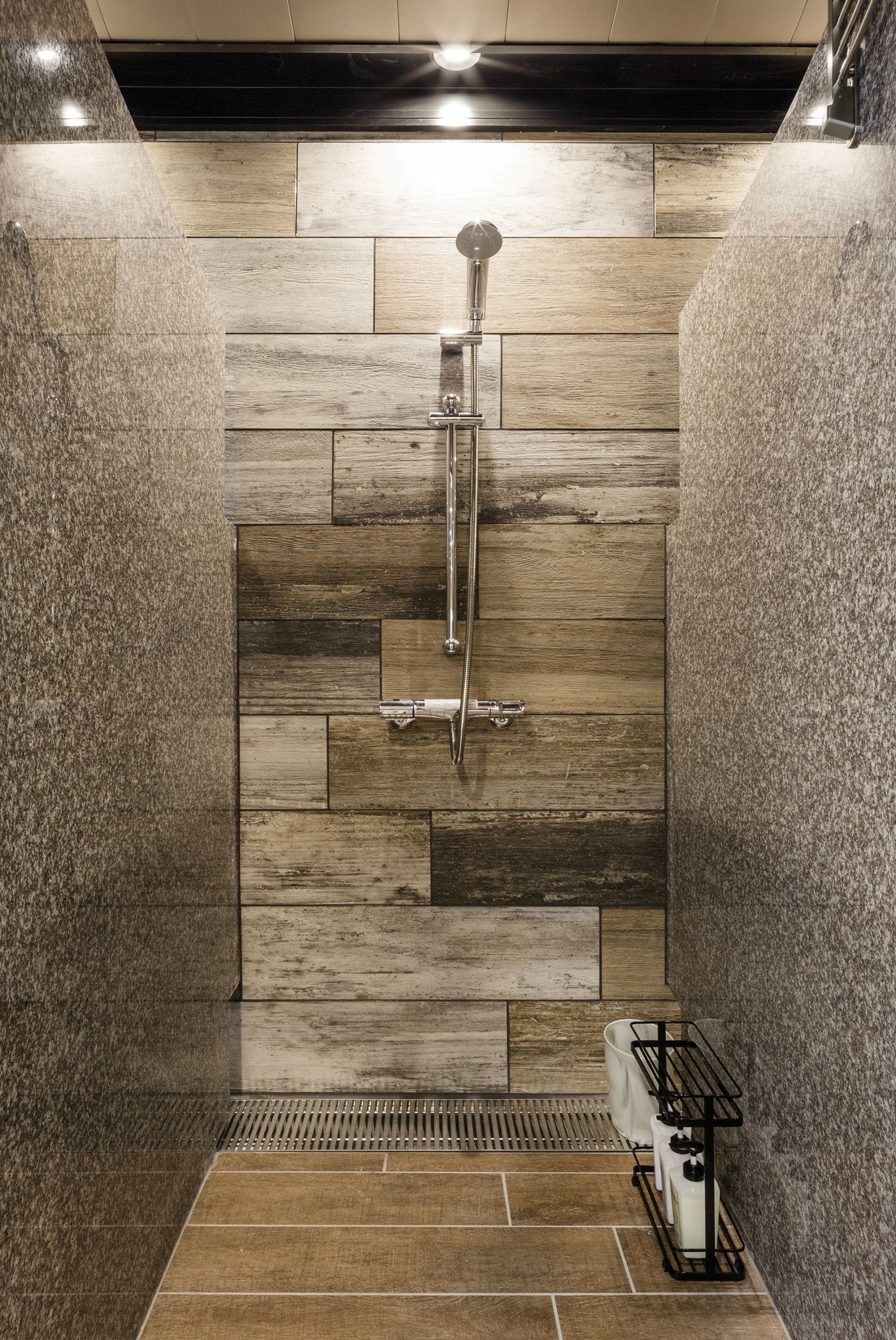 Une douche avec un mur en bois décoratif, un pommeau de douche à main et un robinet fixé au sol.
