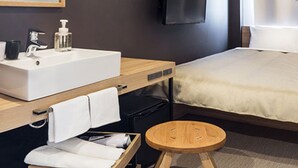 A modern hotel room with a large bed, a bedside table with a sink, a television mounted on the wall, and a small wooden stool. - Sakura Terrace The Atelier (Kyoto)