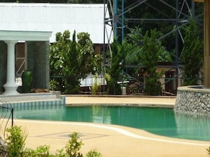 A swimming pool with a stone border, a gazebo, and a building under construction with scaffolding.