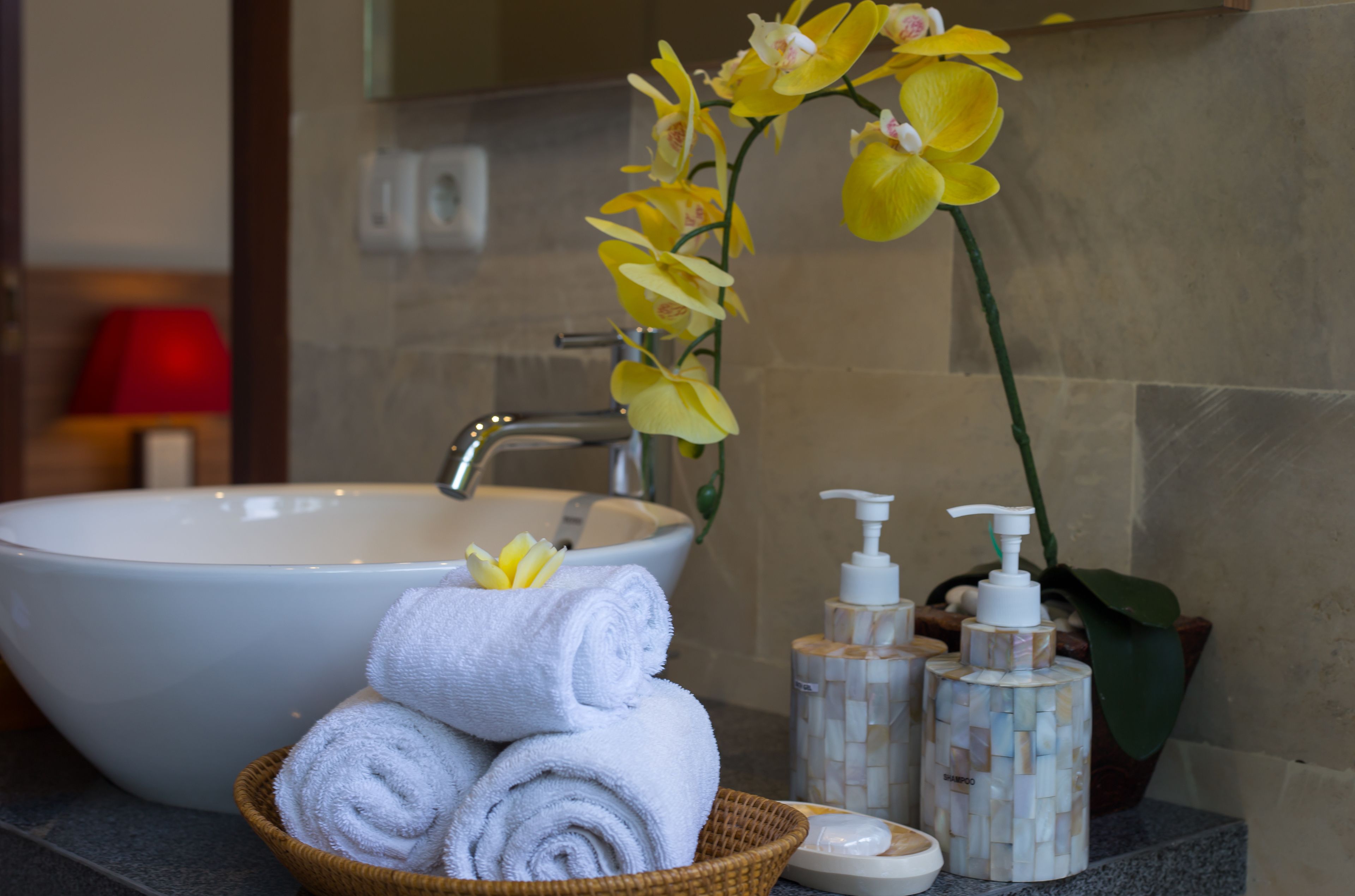 Un baño con un lavamanos grande de color blanco, una cesta de mimbre con toallas enrolladas y dos botellas de artículos de aseo.