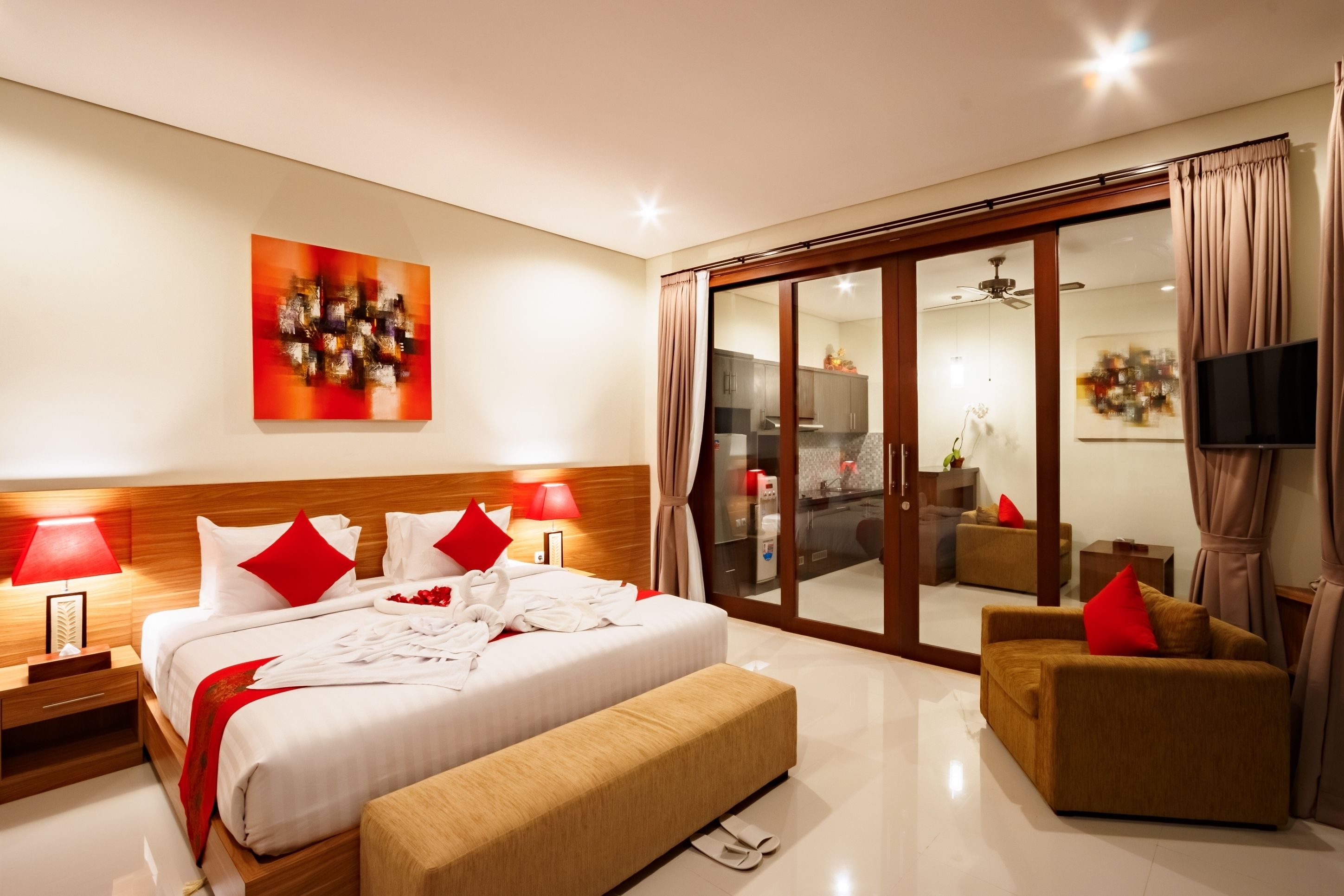 A modern hotel room with a large bed, a sofa, a TV, and a sliding glass door leading to a balcony.