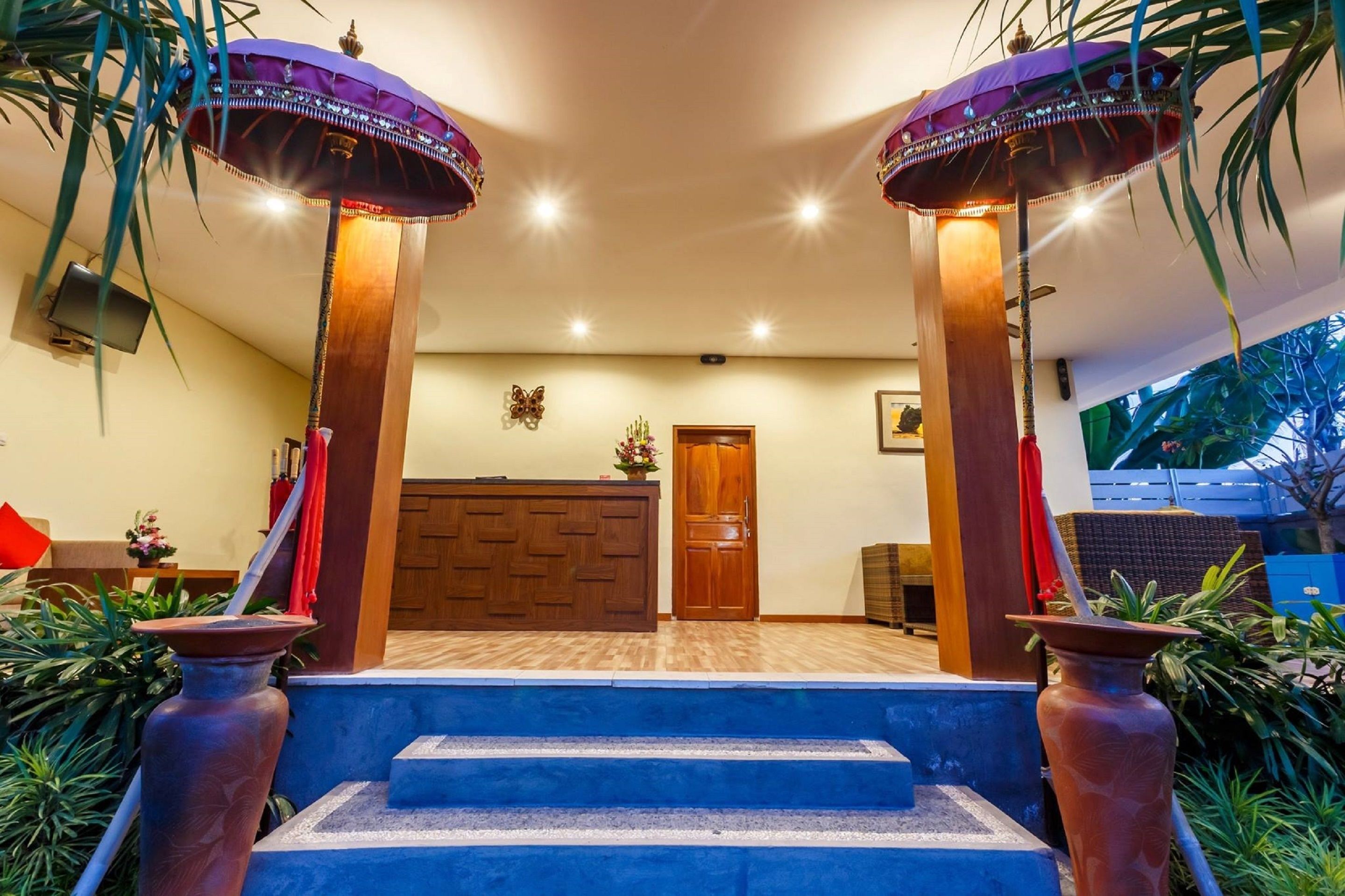 A hotel lobby with a reception desk, a wooden door, and a staircase leading to the upper floor.