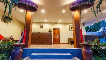 A hotel lobby with a reception desk, a wooden door, and a staircase leading to the upper floor.