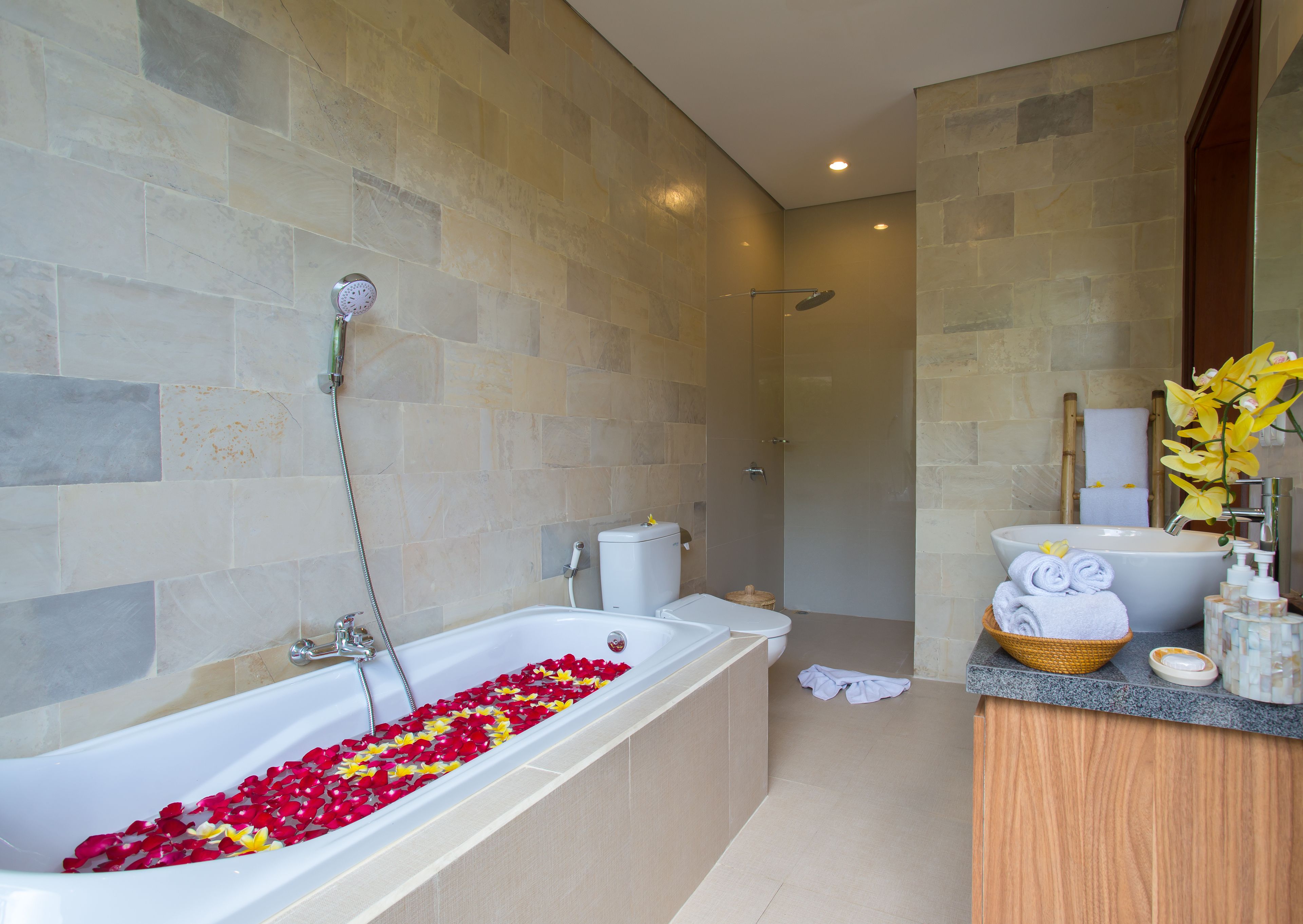 Un baño moderno con una bañera llena de pétalos de rosa, una zona de ducha y un tocador con artículos de aseo.