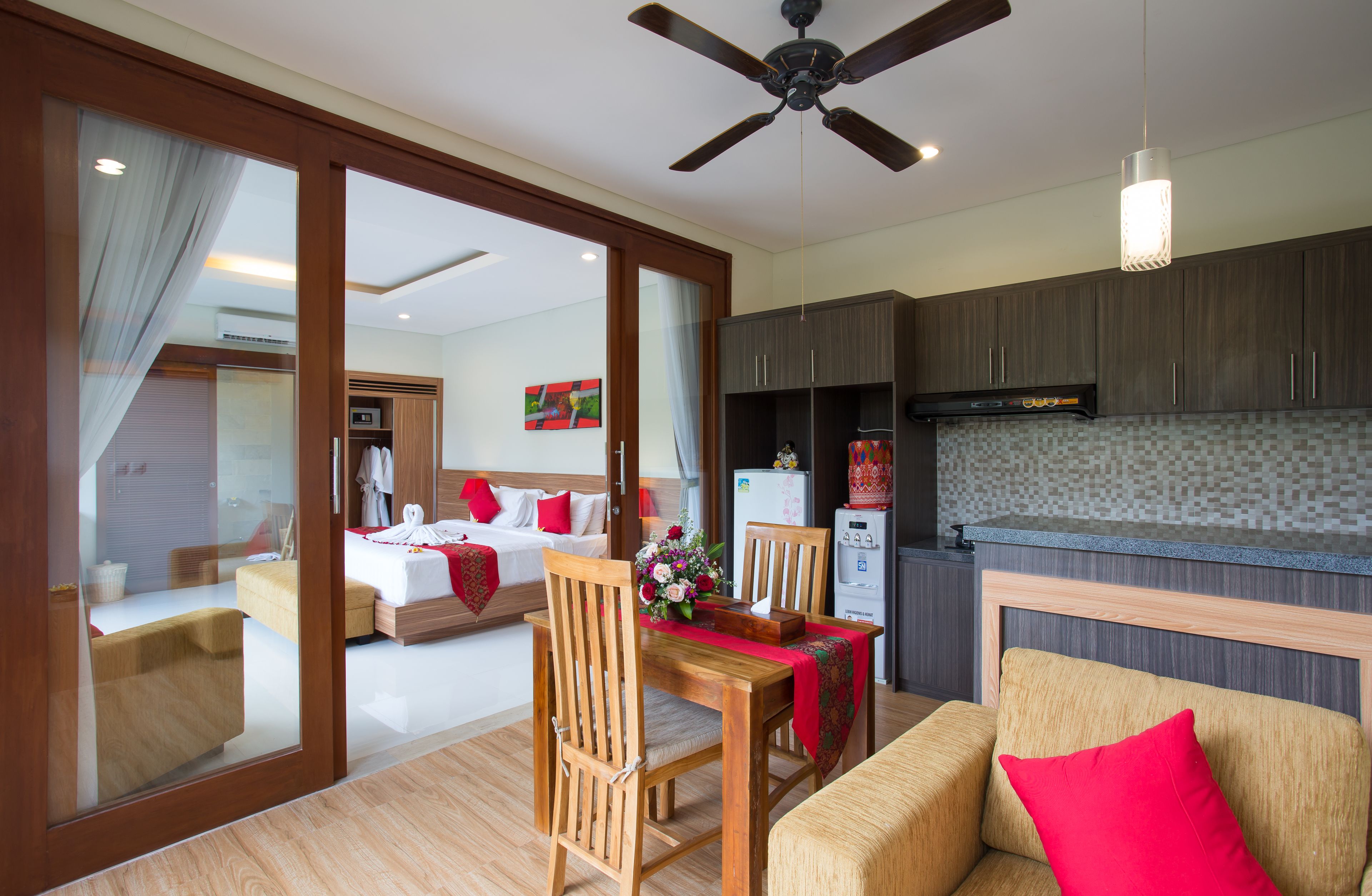 A hotel room with a dining area, a kitchenette, and a bedroom with a bed and a nightstand.