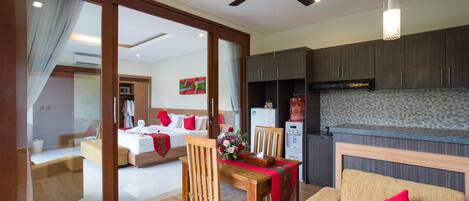 A hotel room with a dining area, a kitchenette, and a bedroom with a bed and a nightstand.