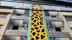 Fachada de hotel com um painel vertical amarelo e azul característico, com arte abstrata detalhada.
