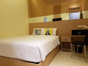 Ein Hotelzimmer mit einem Einzelbett, einem Nachttisch, einem Schreibtisch mit Stuhl und einem Spiegel an der Wand.