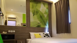 Quarto de hotel com cama, escrivaninha com telefone, uma cadeira e espelho fixado na parede.