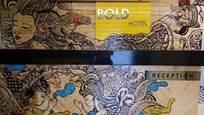 Uma área de recepção de hotel com um letreiro que diz 'WELCOME' e a marca 'BOLD HOTEL'.