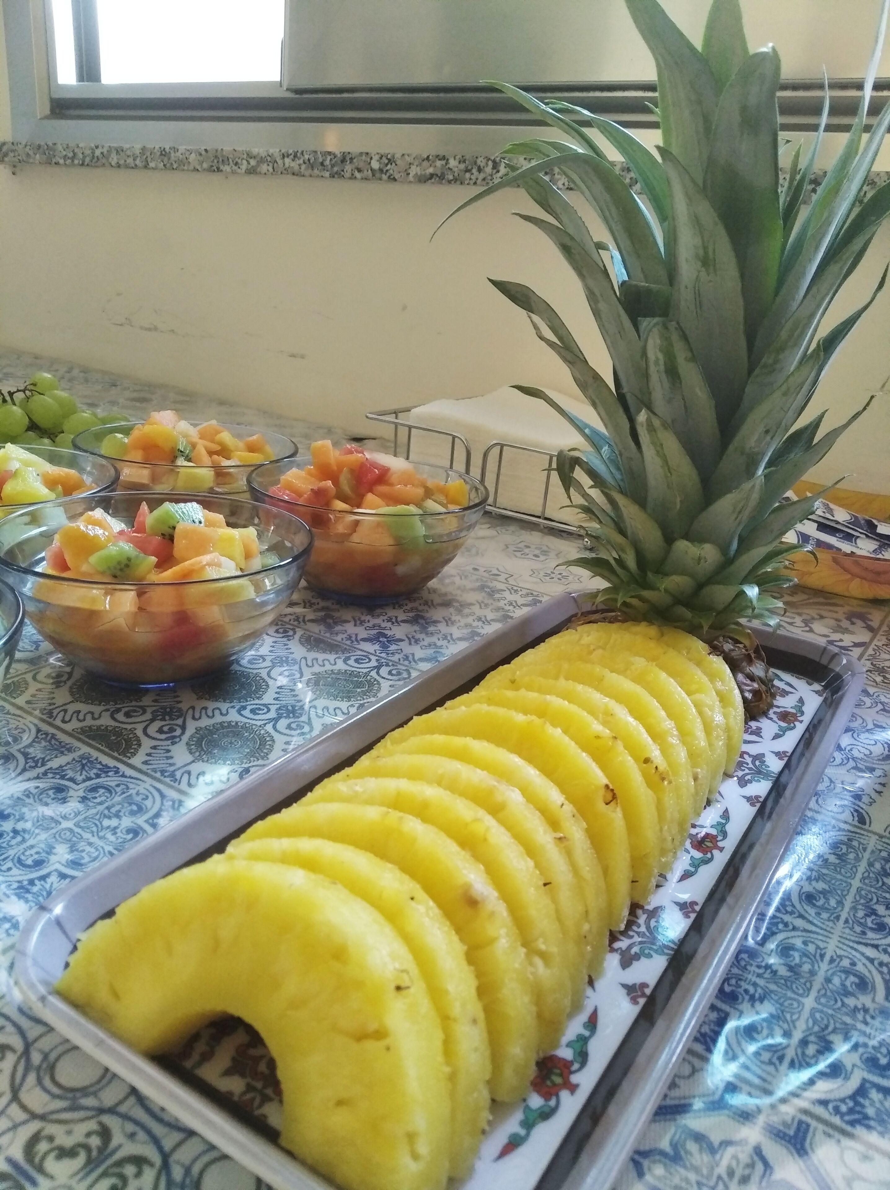 Una bandeja con rodajas de piña y ensaladas de frutas sobre un mantel estampado.