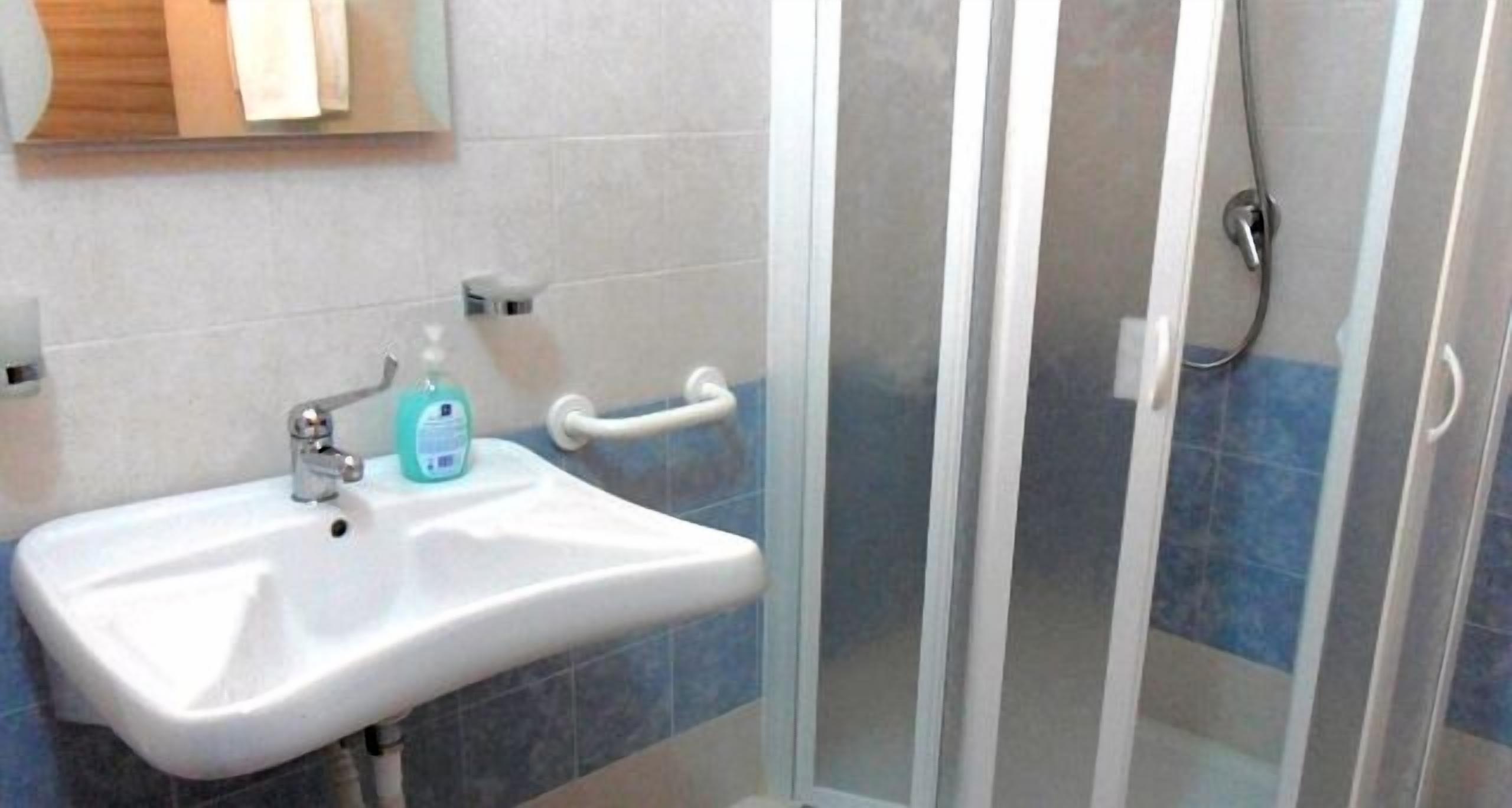 Een badkamer met een witte wasbak, een zeepdispenser en een douchecabine van glas.