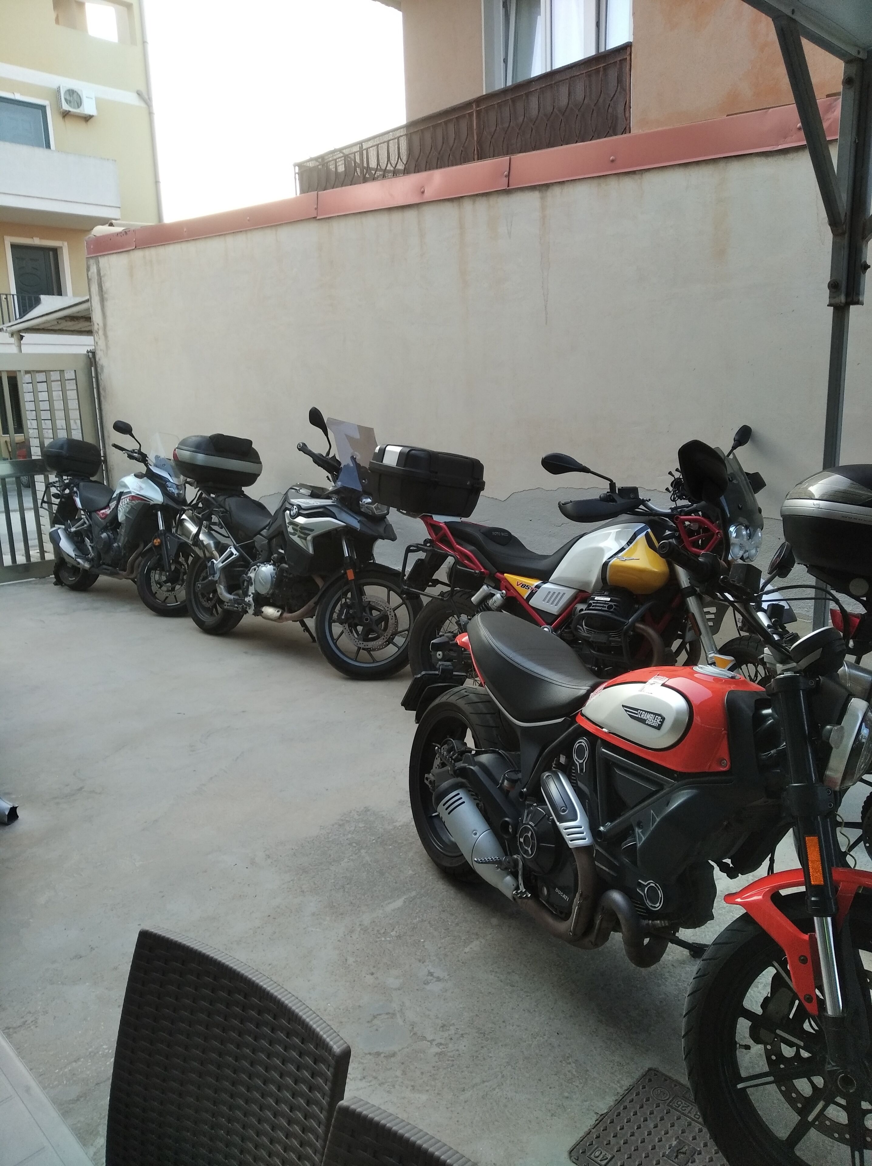 A row of motorcycles parked against a wall in a covered outdoor area.