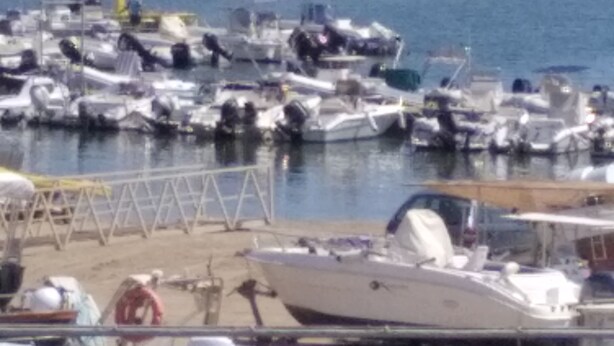 Un puerto deportivo con varias embarcaciones amarradas, una orilla arenosa y una vista despejada del mar.
