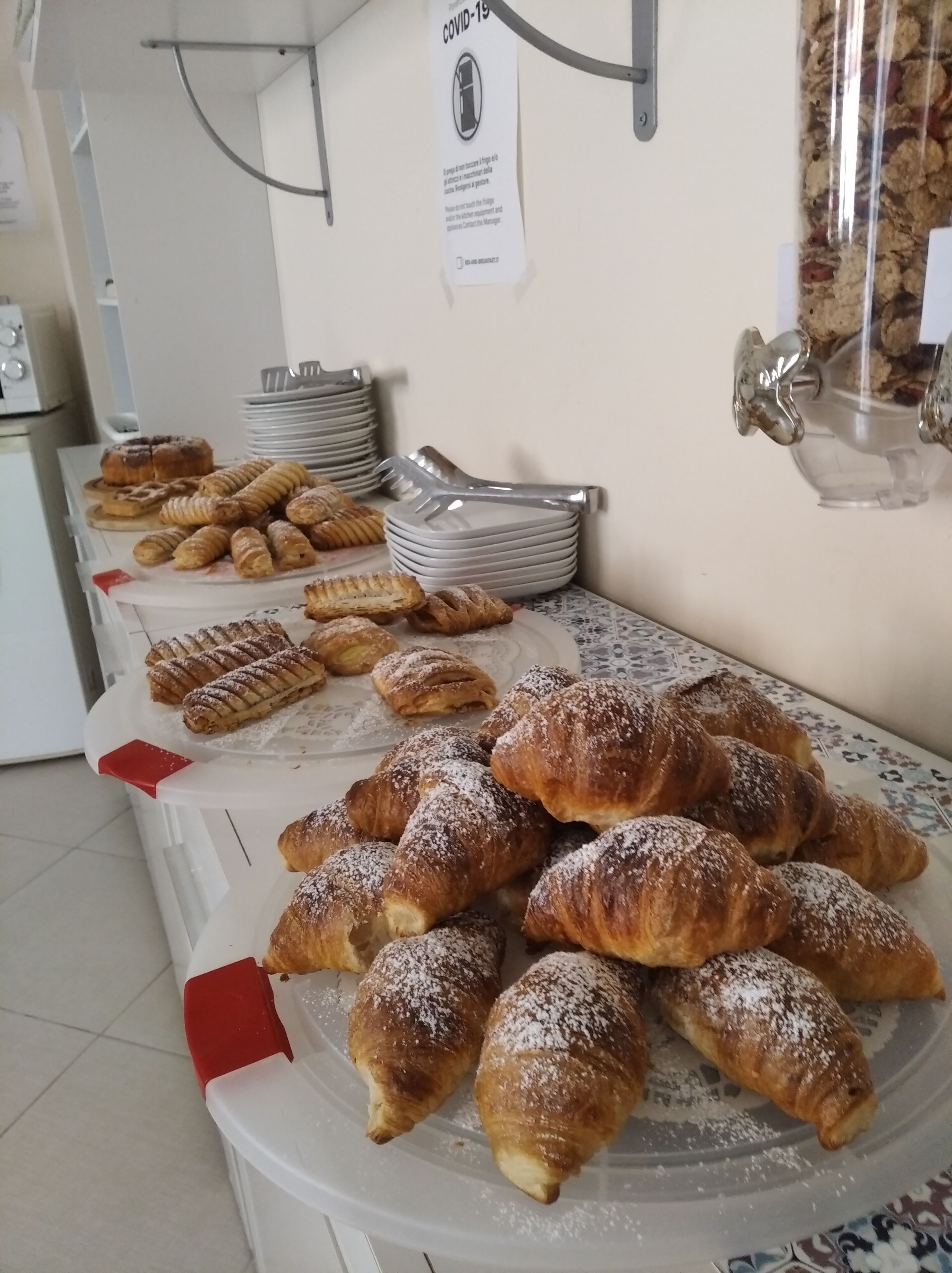 A buffet with various pastries and a sign indicating COVID-19 precautions.