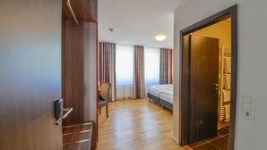 A hotel room with a wooden floor, a bed, a chair, and a window with curtains. - City Hotel Wetzlar (Wetzlar)