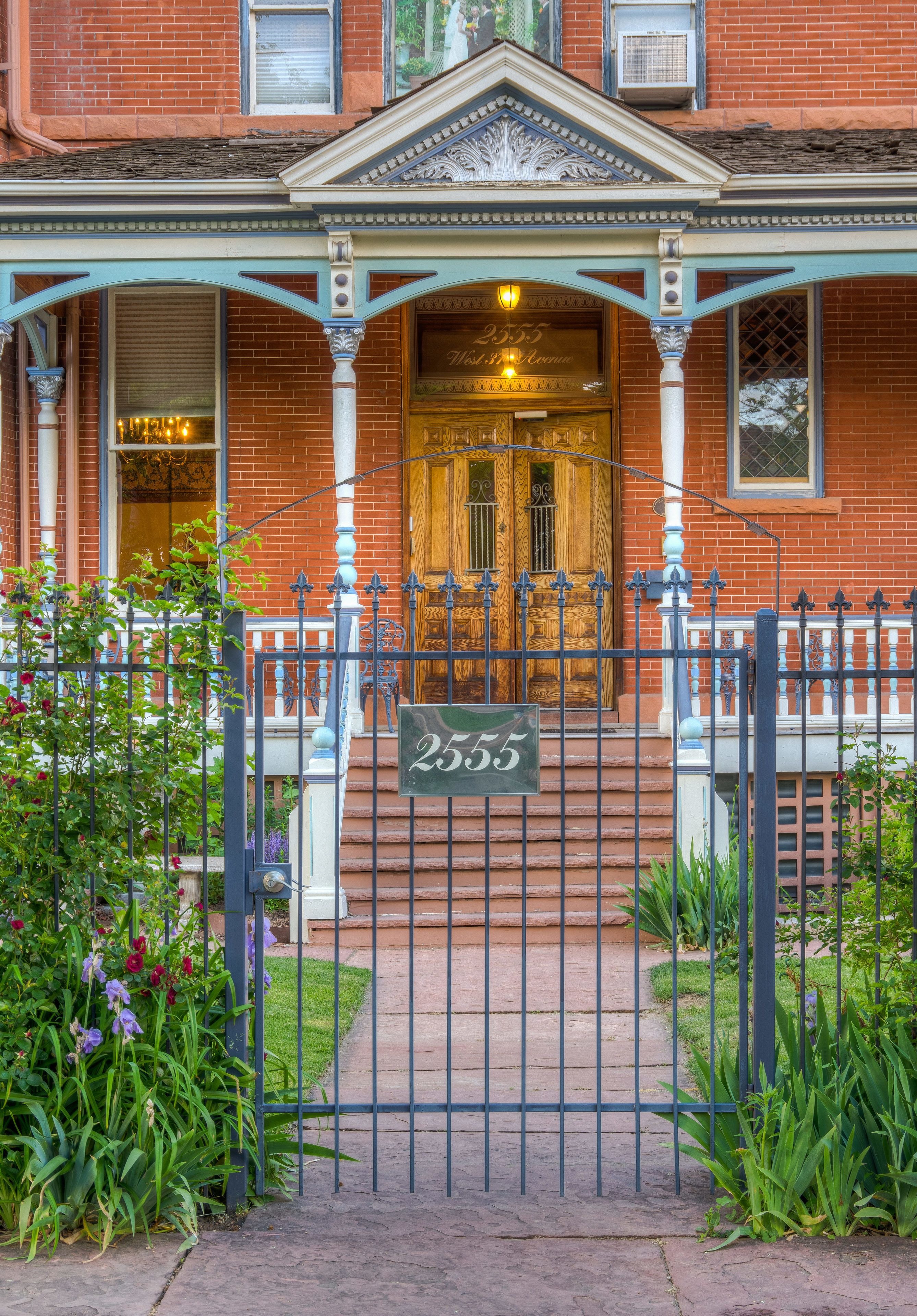 A brick building with a wooden front door, a sign with the number 2555, and a metal gate.