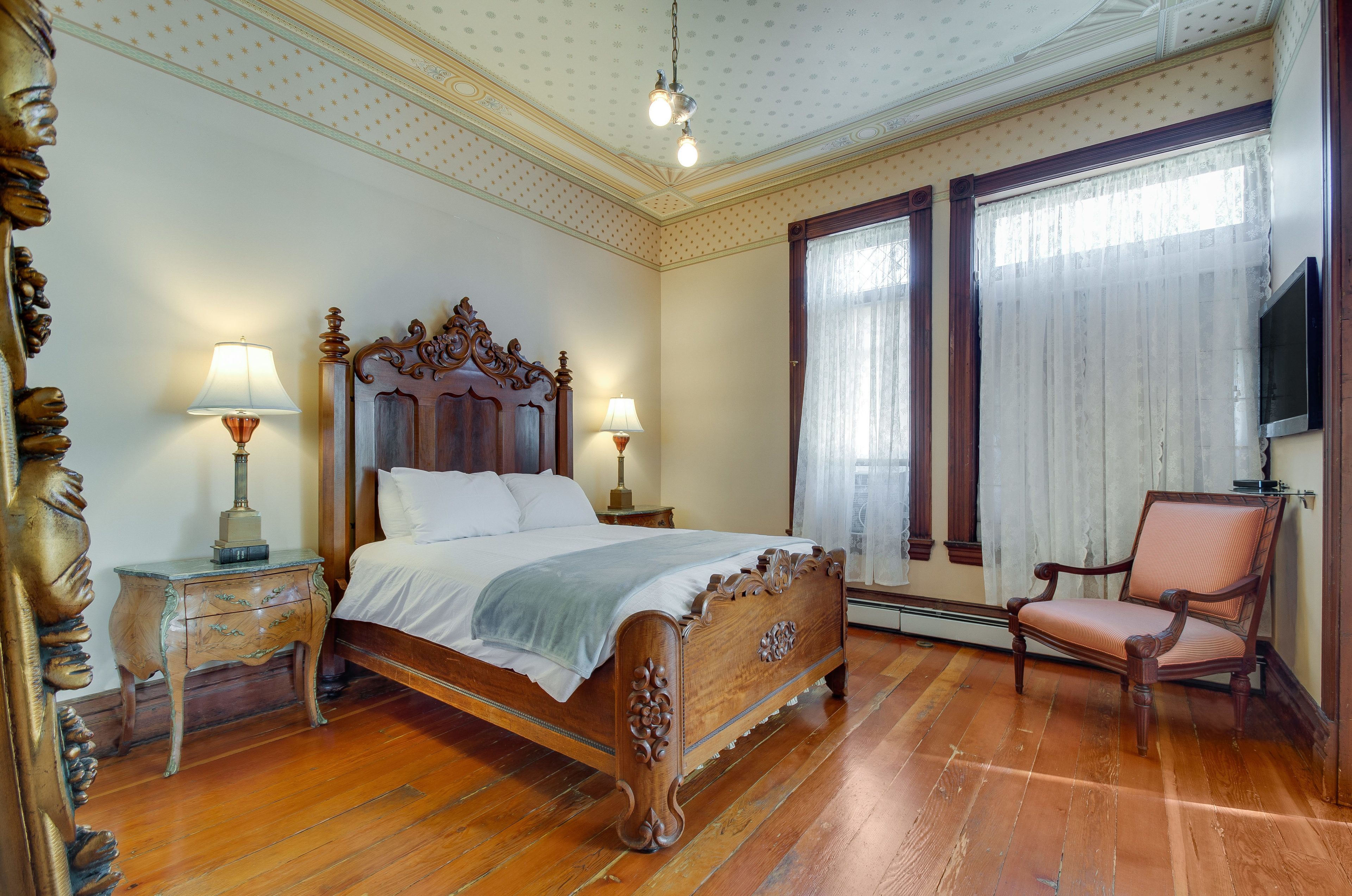 A classic bedroom with a wooden bed, two bedside tables with lamps, a chair, and a television.