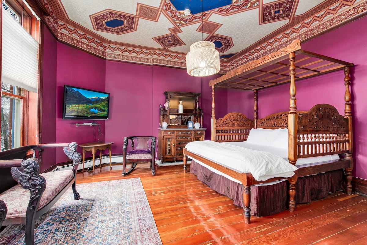 A room with a four-poster bed, a television, a wooden dresser, and a chair.