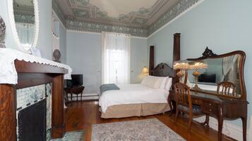 A bedroom with a bed, a desk, a chair, a dresser, a mirror, and a fireplace.