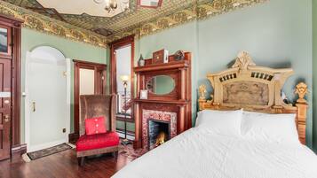 Un dormitorio con una cama grande, una chimenea, un sillón con un cojín rojo y un cabecero de madera.